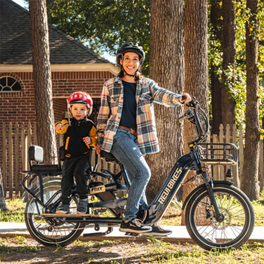 Bike with a smiling adult and child on the rear rack with a cushion