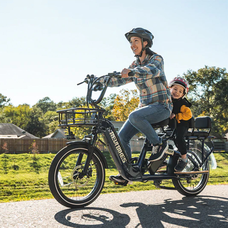 Adult riding the bike on a sunny day with child on rear rack with cushions